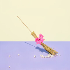 Creative fashion look of a witch's broom with a pink bow and beads, on a pastel yellow and lilac background. Surreal idea, holiday trendy concept for Halloween and autumn..bow
