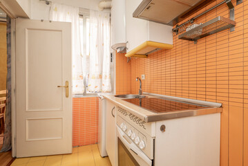 Fototapeta na wymiar Cheap kitchen with white furniture and yellow details, broken appliances and stoneware floors with a white wooden door