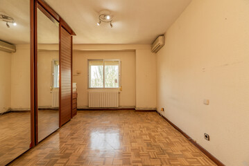 empty room with gleaming oak parquet flooring, wall mounted air conditioner unit and three sliding mirror and venetian door wardrobe