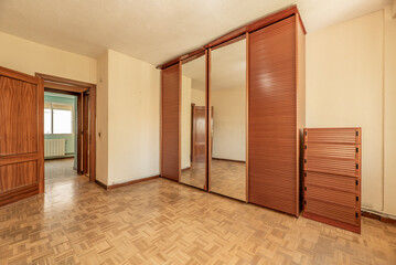 empty room with gleaming oak parquet floor, chest of drawers and three sliding mirrors and wardrobe with venetian door