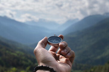 Magnetic compass in the palm of a male hand against the backdrop of a mountain range in the clouds...