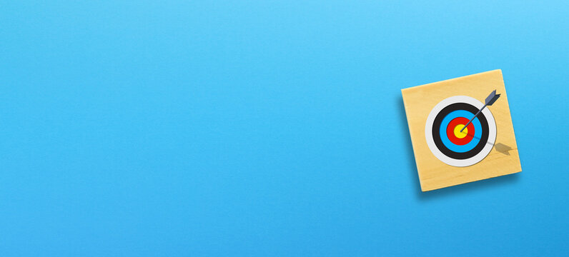 Target dartboard on wooden cube block with blue background