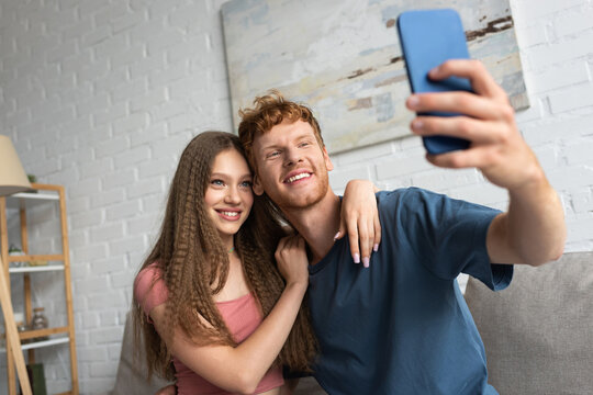 young and happy man taking selfie with positive girlfriend in living room.