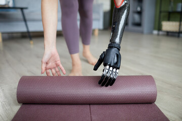 Close-up of young woman with prosthetic arm using exercise mat in her training at home - obrazy, fototapety, plakaty