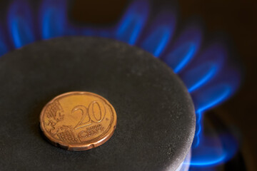 Close-up of 20 cent coin on gas stove burner with flame, as natural gas price increase concept