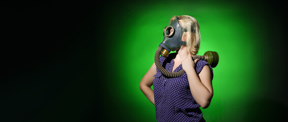 blonde woman in a gas mask stands sideways and looks away at an empty space for text on a dark background