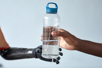 Close-up of African man giving bottle of water to woman with prosthetic arm isolated on blue...