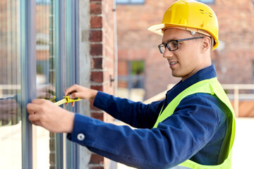 Fototapeta na wymiar construction business and building concept - happy smiling male builder with ruler measuring window