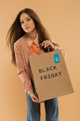 teenage girl holding paper bag with black friday lettering isolated on beige.