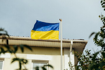 The flag of Ukraine flutters in the wind. It is attached to the facade of the house under the window.