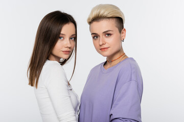 brunette and blonde lesbian couple with makeup looking at camera isolated on grey.