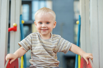Cute two year old boy plays on playground slide on summer. Active kid on colorful slide and swing.