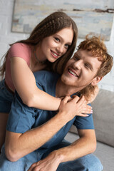 happy teen girl smiling and hugging redhead boyfriend in living room.