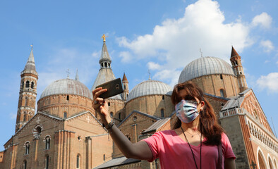 young woman with surgical mask taking a photo with smartphone in Padua and the Basilica of Saint...