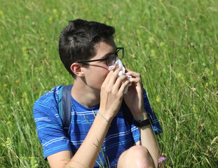 young boy with glasses blowing his nose because of allergy in the meadow