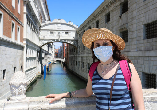 young female tourist with big straw hat surgical mask and in the background the very famous Bridge of Sighs in Venice in Italy