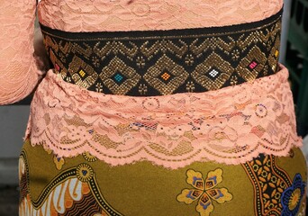 Rücken von indonesischer Frau mit pinkem Spitzenoberteil und schwarzer dicker Borte mit goldenem...