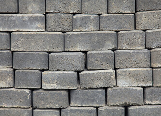 Fototapeta premium The surface of a wall or fence lined with gray bricks. Paving slabs of grey blocks of flat shape. Pavement blocks in city park. Park way materials. Bricks or blocks of paving slabs laid in row