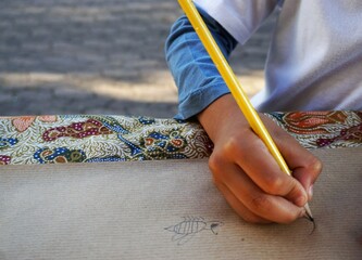 Kinderhand von Jungem beim Malen mit gelbem Bleistift auf Papppapier auf Tisch in Stadt bei Sonne...