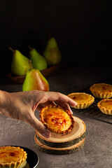 A hand reaching for a freshly baked tart, with juicy pears in the background, evoking a sense of homely baking tradition