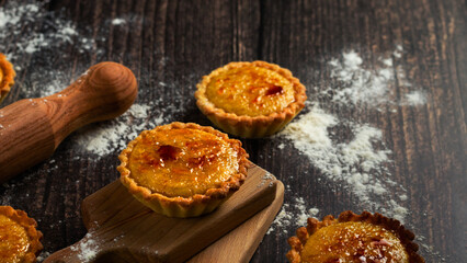 A close-up of scrumptious tarts on a wooden board, the flour and rolling pin hinting at the joy of...