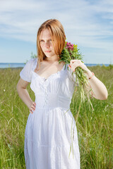 Beautiful girl in a white dress with flowers in a field overlooking the sky