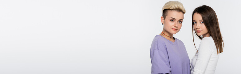 blonde and brunette lesbian women looking at camera isolated on grey, banner.