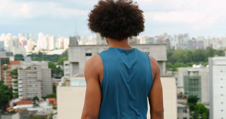 Young black african man overlooking city view on top of rooftop, turning head towards camera with serious dramatic expression portrait - Powered by Adobe