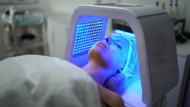 Young woman having red and blue LED light facial therapy treatment in beauty salon while laying on a couch and relaxing. Beauty, healthcare and wellness concept.