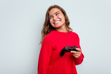 Young caucasian gamer woman holding a game controller isolated on blue background looks aside smiling, cheerful and pleasant. © Asier
