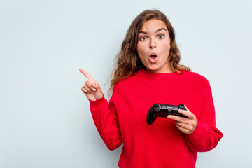 Young caucasian gamer woman holding a game controller isolated on blue background pointing to the...