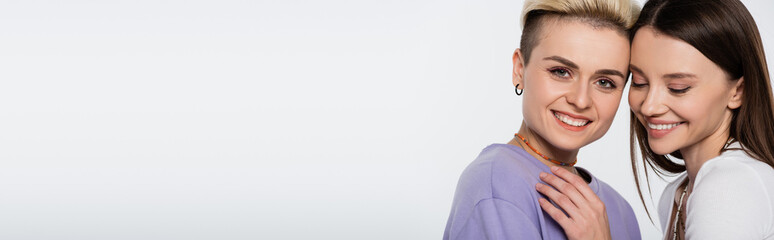 young lesbian couple with makeup smiling isolated on grey, banner.