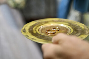 During a church wedding, gold wedding rings are held on a tray in the hands.