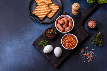 Traditional English breakfast with eggs, toast, sausages, beans, spices and herbs on a grey ceramic plate