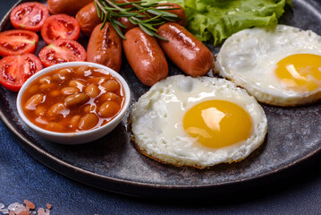 Traditional English breakfast with eggs, toast, sausages, beans, spices and herbs on a grey ceramic plate