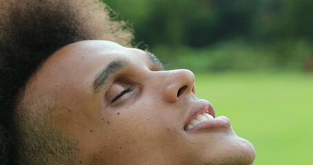 Young african man closing and opening eyes, looking up to sky with faith and hope