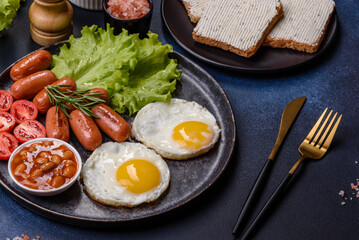 Traditional English breakfast with eggs, toast, sausages, beans, spices and herbs on a grey ceramic plate
