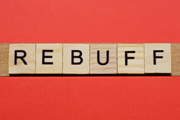 text the word rebuff from gray wooden small letters with black font on an red table