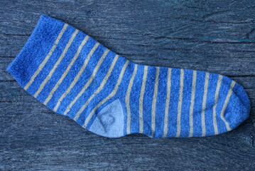one old woolen striped blue yellow sock lying on a gray wooden table