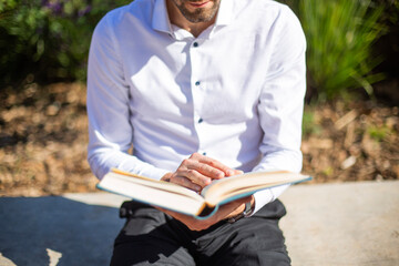 Closeup view of young man reading the bible. Young man with the bible at a park sitting on a bench. Horizontal.