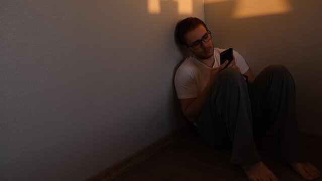 alone depressed man sitting in corner dark room because of problem and sadness in life cheking his phone. Sadnes and spite concept