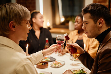 Happy young homosexual couple clinking with alcoholic drinks by dinner table served with homemade food against lesbian couple