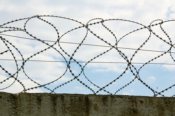 Barbed wire on the fence. Fencing stainless steel Barb Wire with sharp edges on a massive concrete wall for security on the background a blue sky. Military barbwire fence. Barbwire on the prison fence