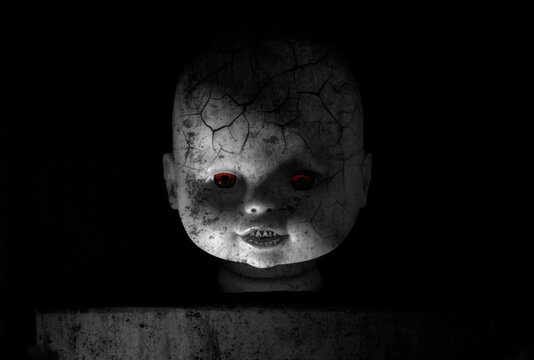 Zombie doll portrait. Creepy of doll face with glowing red eyes and zombie skin in the black background. Halloween concept.
