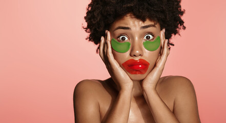 African american beauty girl with funny under eye and lips patches for skincare, looking surprised, shocked face, standing over pink background
