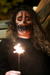 Close up of a woman wearing halloween makeup at night. Young woman in halloween makeup with a roman candle at night