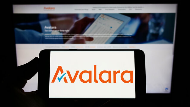 Stuttgart, Germany - 09-08-2022: Person holding smartphone with logo of US software company Avalara Inc. on screen in front of website. Focus on phone display.