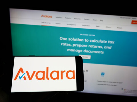 Stuttgart, Germany - 09-08-2022: Person holding mobile phone with logo of American software company Avalara Inc. on screen in front of business web page. Focus on phone display.