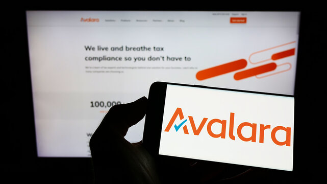 Stuttgart, Germany - 09-08-2022: Person holding cellphone with logo of US software company Avalara Inc. on screen in front of business webpage. Focus on phone display.