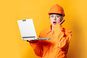 woman construction worker in helmet and orange overalls holding a laptop